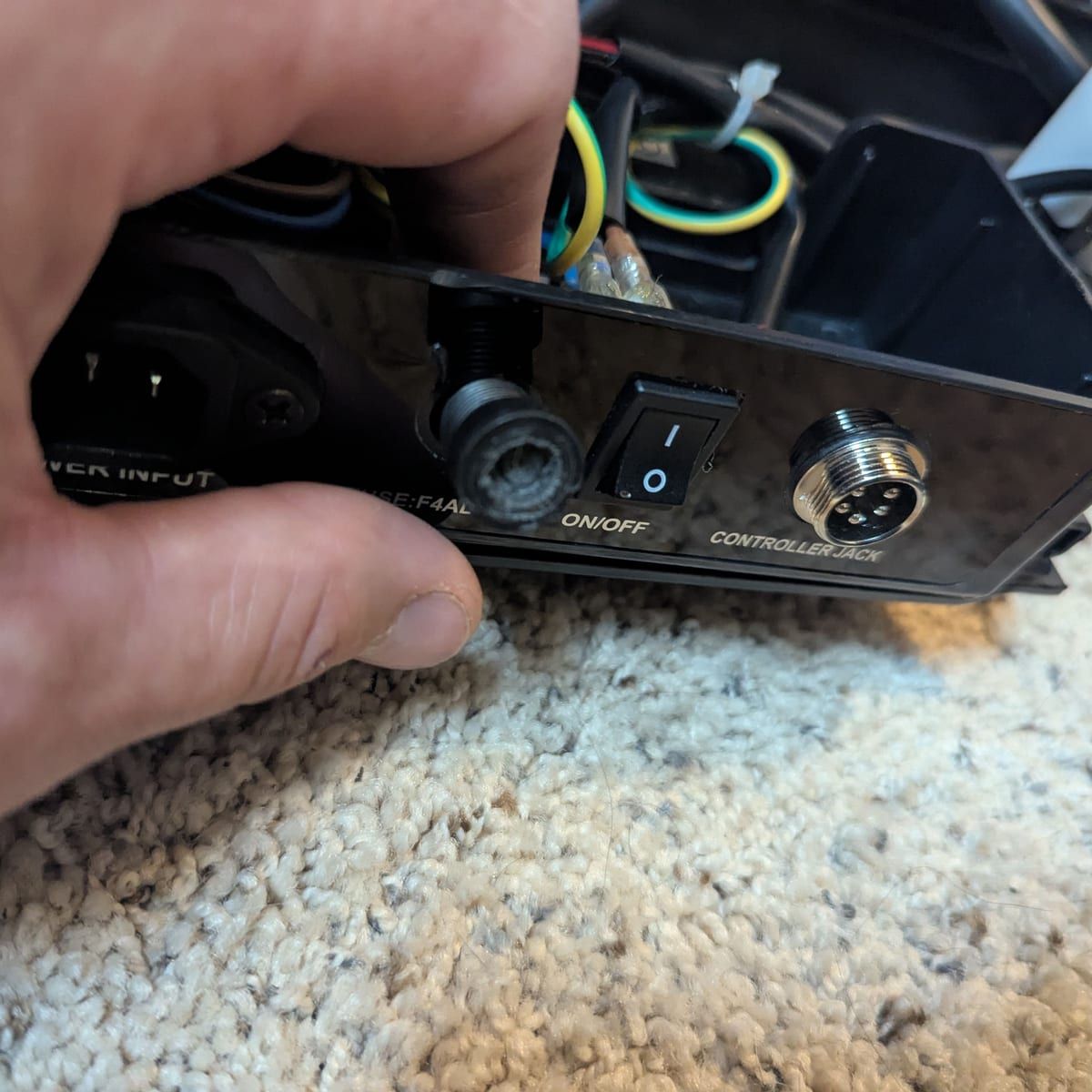 A technician holds a massage chair's control box, showing the power input, fuse, on/off switch and controller jack.