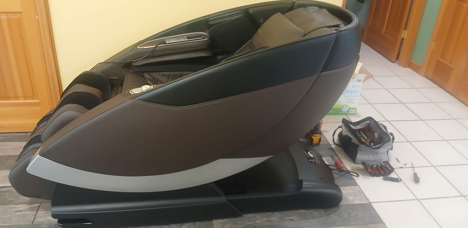 A repaired massage chair, back together, with the technician's tool bag on the floor beside it.
