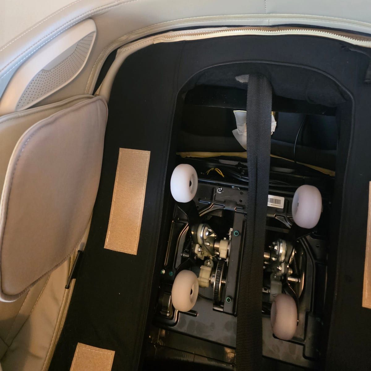 The back of a massage chair unzipped to show the roller mechanism and its four rollers.