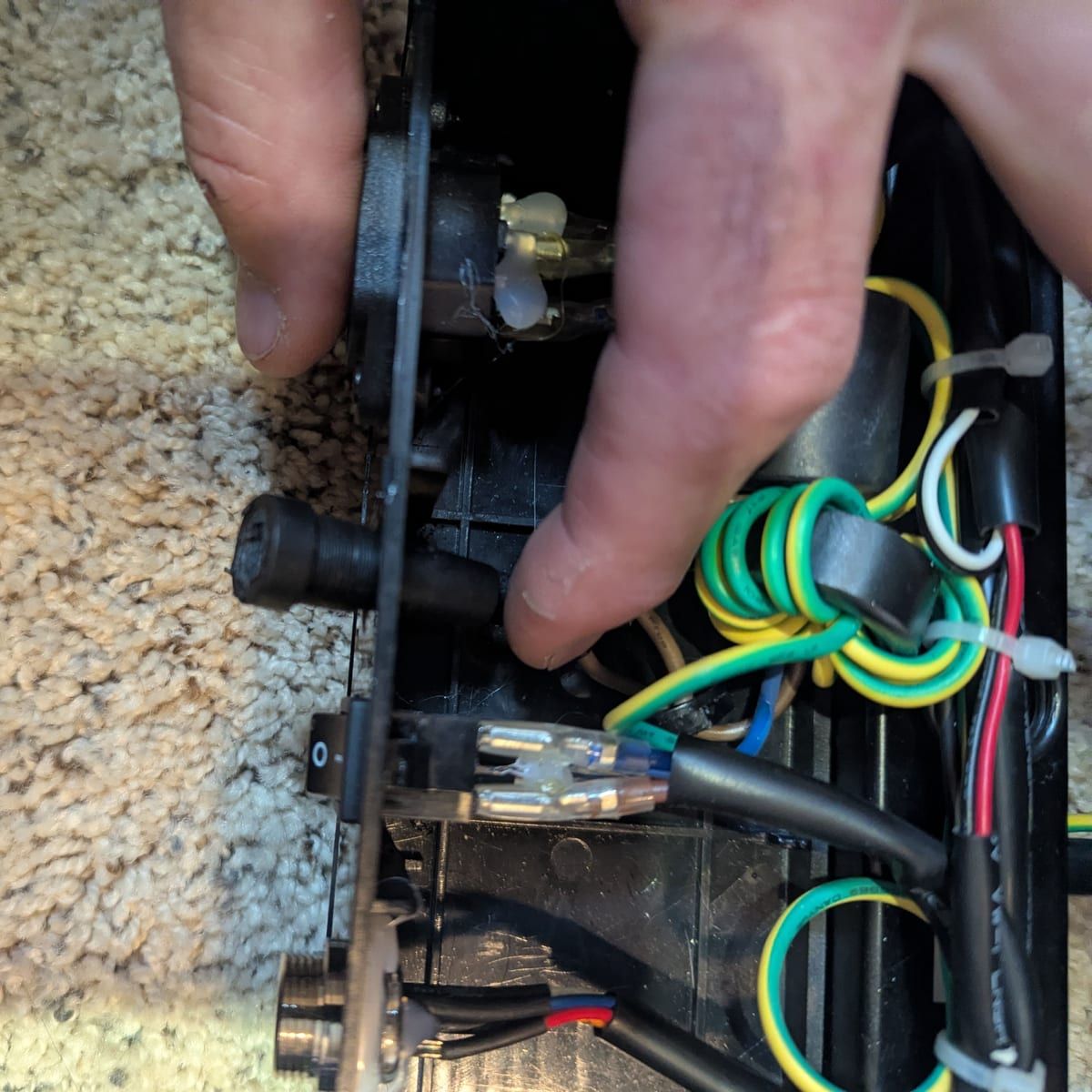 A technician's hands at work on the wiring inside a massage chair's control box.